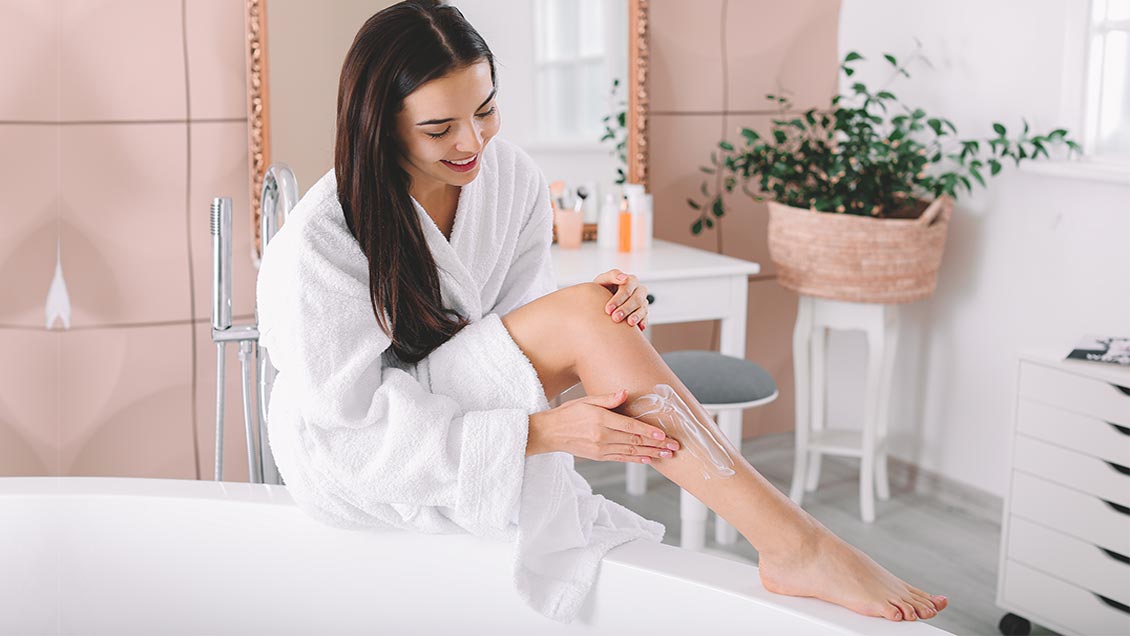 woman applying aftershave lotion on legs after shaving